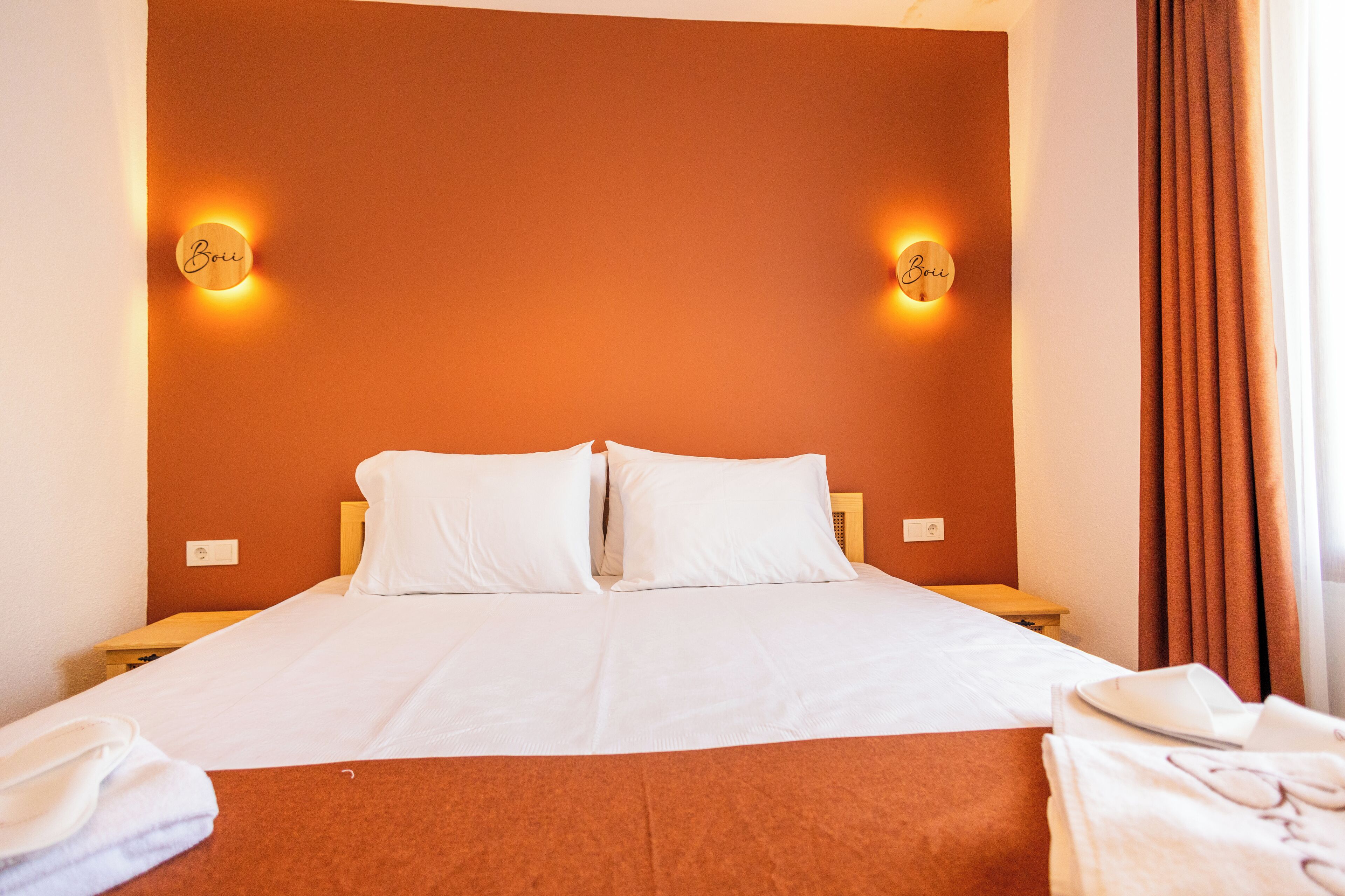 A hotel room with a large bed, two bedside tables, a nightstand, and a window with curtains.
