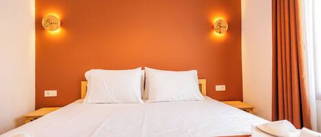A hotel room with a large bed, two bedside tables, a nightstand, and a window with curtains.