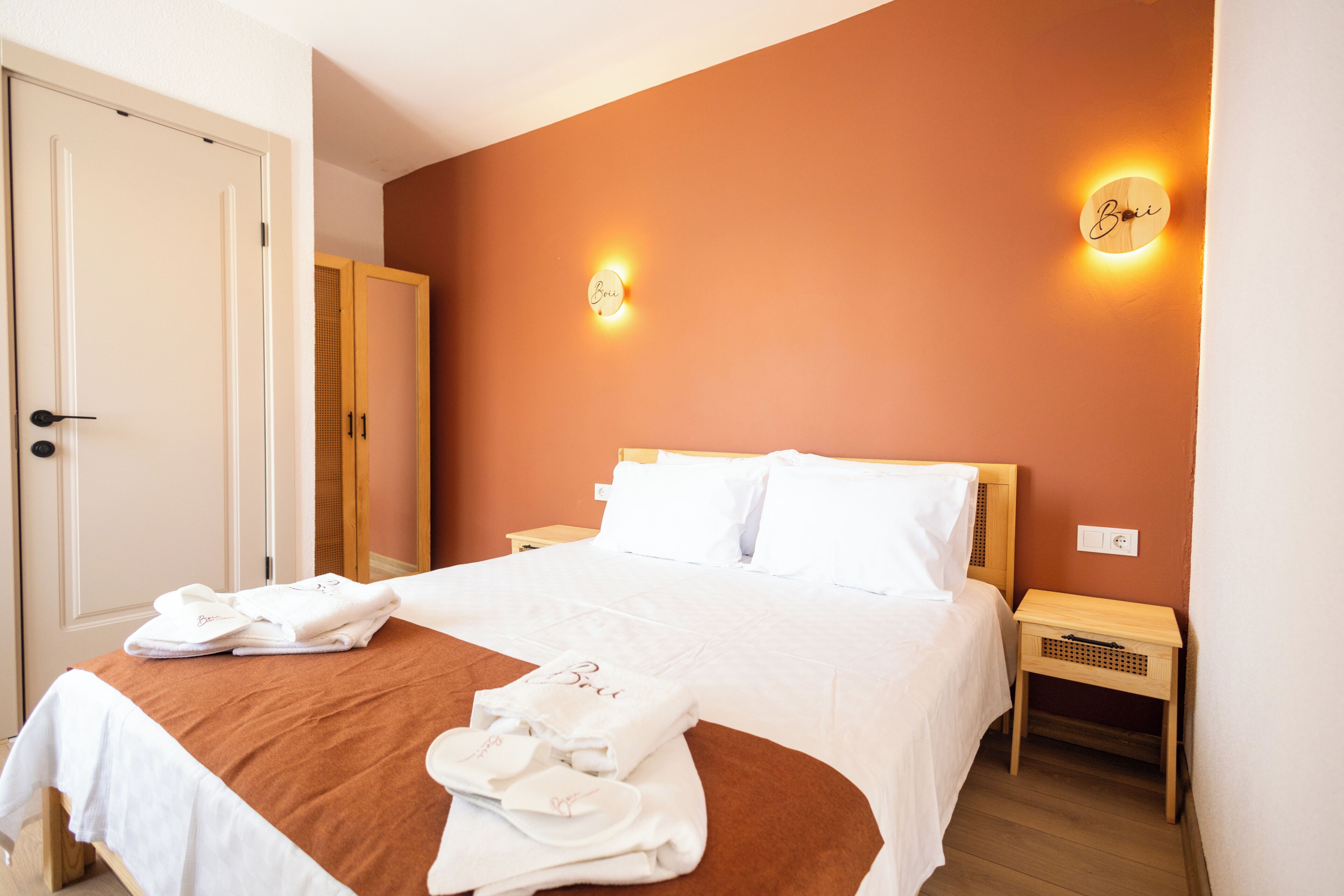 A hotel room with a bed, two bedside tables, a wardrobe, and a door.