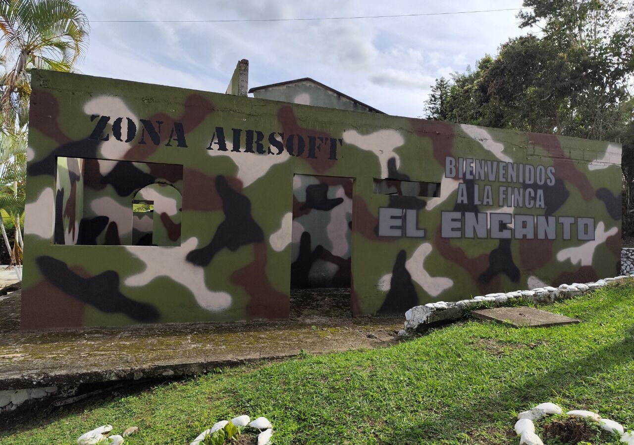 Ein Gebäude mit Tarnmustern und Schildern mit der Aufschrift "Zona Airsoft" und "Bienvenidos a la finca El Encanto".