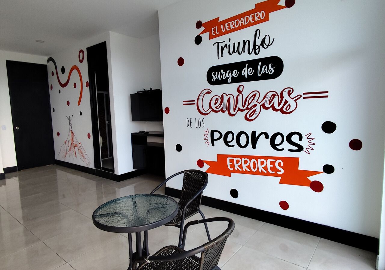 Un interior moderno con un mural en la pared, una mesa redonda de cristal y sillas de mimbre negro.