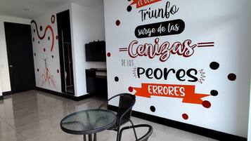 Un interior moderno con un mural en la pared, una mesa redonda de cristal y sillas de mimbre negro.