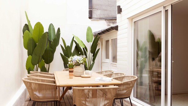 A patio with a wooden table and wicker chairs, surrounded by large green plants. - Maison Legendre - Luxury Townhouse with 5BDR & AC in Batignolles (Paris)