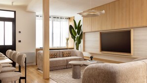 A modern living room with a sofa, a dining table with chairs, a coffee table, a large TV, and a plant. - Maison Legendre - Luxury Townhouse with 5BDR & AC in Batignolles (Paris)