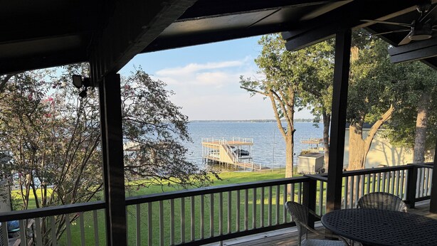 Une terrasse en bois avec une table et des chaises, donnant sur un lac où se trouvent un quai et des bateaux.