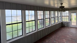 Une pièce dotée de grandes fenêtres, d’un sol en briques et d’un ventilateur de plafond.