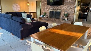 Un salon avec un canapé, une table à manger en bois et un téléviseur fixé au mur en briques.