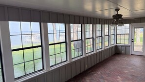 Une pièce dotée de grandes fenêtres, d’un plancher en briques et d’un ventilateur de plafond.