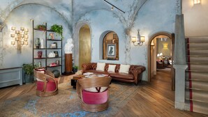 Un amplio salón con un sofá de cuero, dos sillones de mimbre, una estantería y un techo decorativo.
