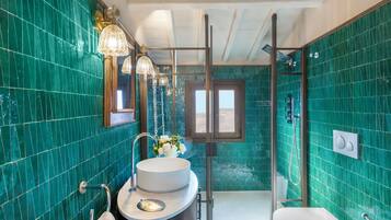 Un baño con un lavamanos grande y redondo, una cabina de ducha de cristal y un espejo con marco dorado.