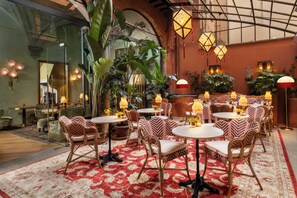 A cozy indoor dining area with round tables and cushioned chairs, surrounded by lush plants and warm lighting. - The James Suite Hotel Firenze 1564 - Small Luxury Hotels of the World (Florence)