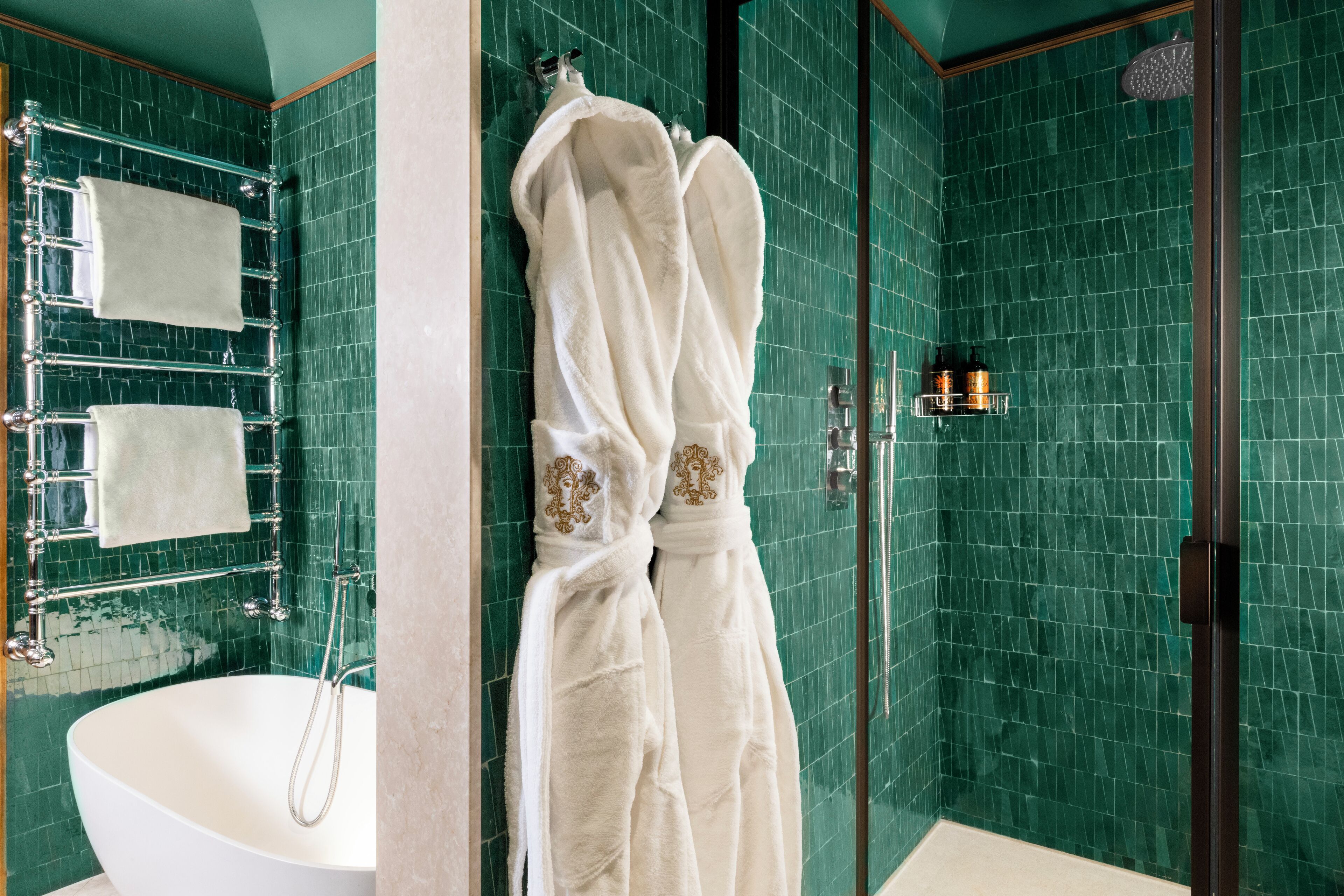 Un baño con una bañera independiente, ducha con cerramiento de vidrio y paredes con azulejos verdes.