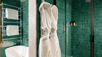Un baño con una bañera independiente, ducha con cerramiento de vidrio y paredes con azulejos verdes.