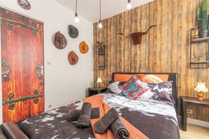 A bedroom with a wooden wall, a bed with a patterned bedspread, and several decorative items including a cow head and hats.