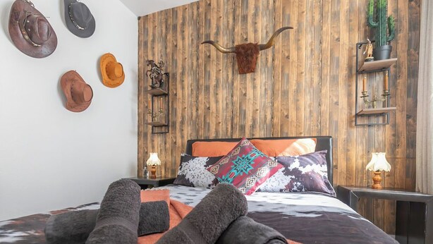 A bedroom with a wooden wall, a bed with patterned pillows, and a collection of hats on the wall. - La Tanière du Cowboy (Orléans)