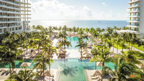 Un resort con una grande piscina circondata da palme, una spiaggia e vista sull'oceano.