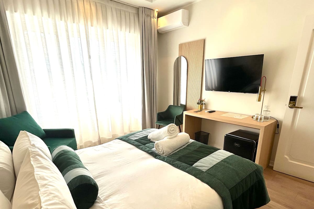 Habitación de hotel con una cama grande, un escritorio, un televisor de pantalla plana y una ventana con cortinas.