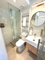 Une salle de bain moderne avec une douche à parois de verre, des toilettes, un lavabo avec un miroir et un porte-serviettes.