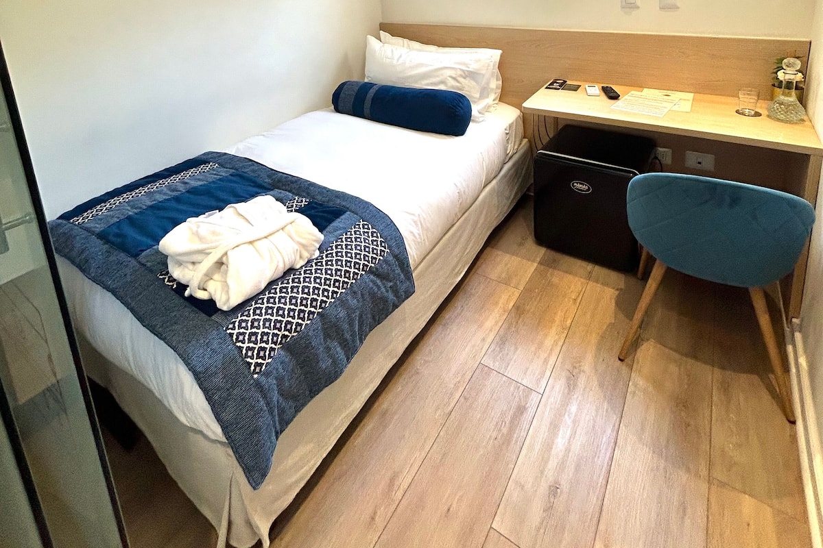 Una habitación de hotel pequeña con una cama, un escritorio y una silla.