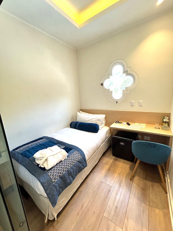 Una habitación de hotel pequeña con una cama, un escritorio y una silla.
