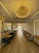 Un hall d’hôtel spacieux, agrémenté d’un lustre central, de coins salon et d’œuvres d’art encadrées qui ornent les murs.
