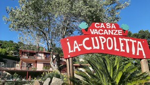Naamplaatje voor 'Casa Vacanze La Cupoletta' met uitzicht op een gebouw en omliggend groen.