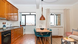 Une cuisine moderne avec des meubles en bois, une table à manger avec des chaises, un luminaire suspendu et une vue par les fenêtres.