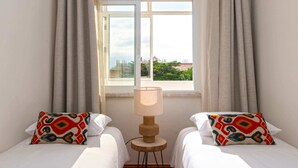 Une chambre d’hôtel avec deux lits, une fenêtre avec des rideaux et une lampe sur une table en bois.