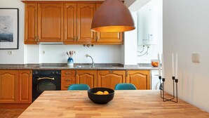 Une cuisine avec des meubles en bois, un four noir, un évier et une table à manger sur laquelle se trouve un saladier rempli de citrons.
