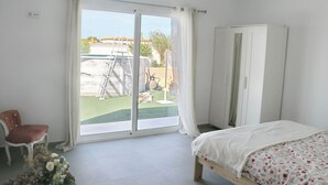 Quarto com cama, uma cadeira, guarda-roupa e porta de vidro deslizante para uma varanda.