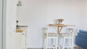 Uma pequena cozinha compacta com pia, uma mesa de madeira com duas cadeiras e um sofá azul.