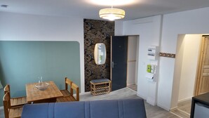 Moderni huone, jossa on puinen ruokapöytä, sininen sohva, pieni puinen jakkara ja seinälle kiinnitetty peili.