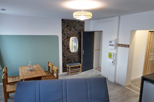 Una habitación moderna con una mesa de comedor de madera, un sofá azul, un taburete pequeño de madera y un espejo montado en la pared.