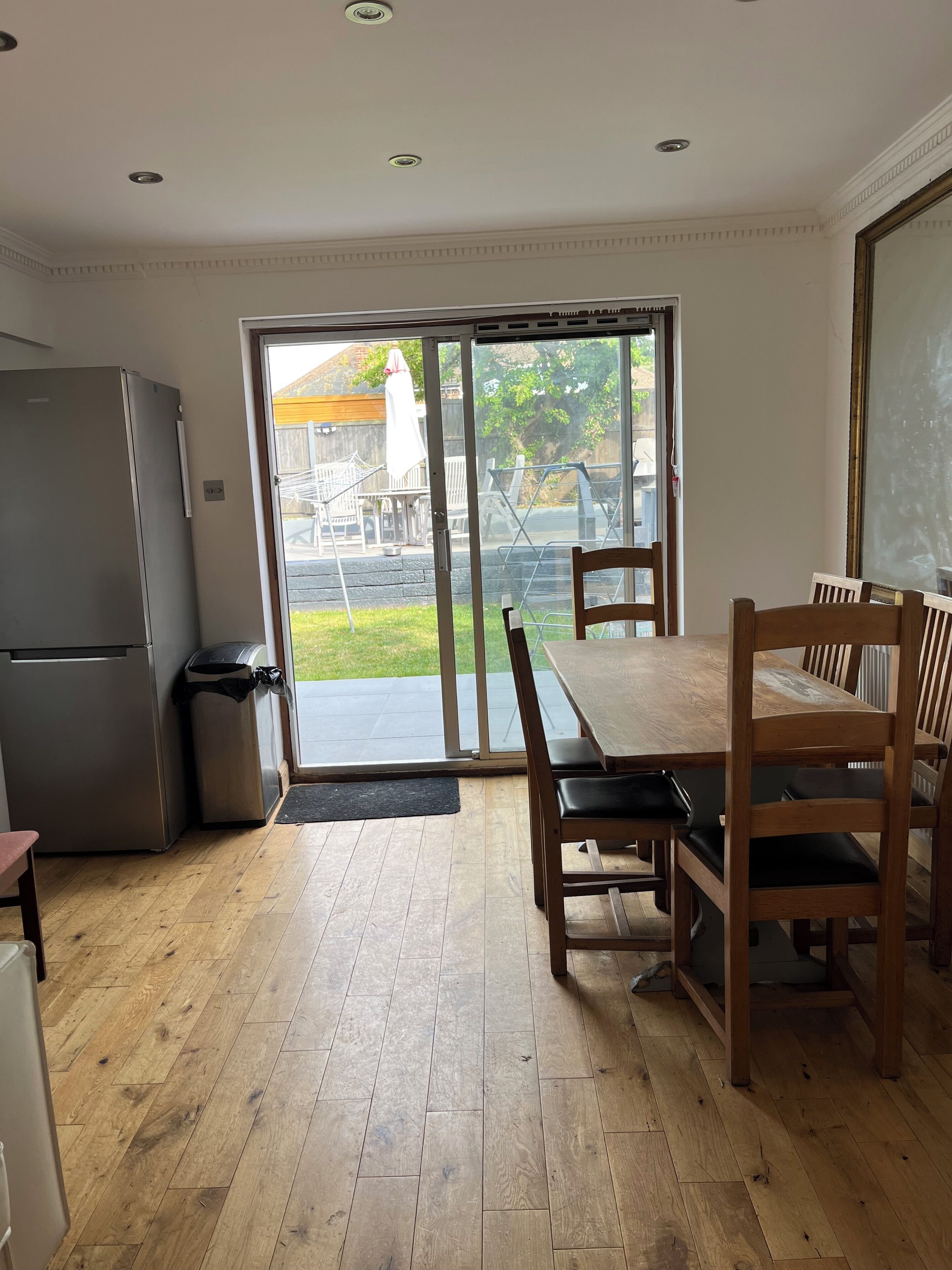 A kitchen with a refrigerator, a trash bin, and a dining area with a table and chairs.