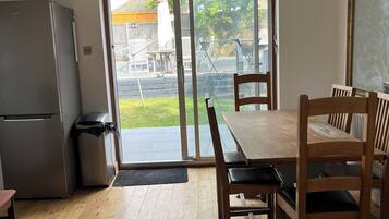 A kitchen with a refrigerator, a trash bin, and a dining area with a table and chairs.