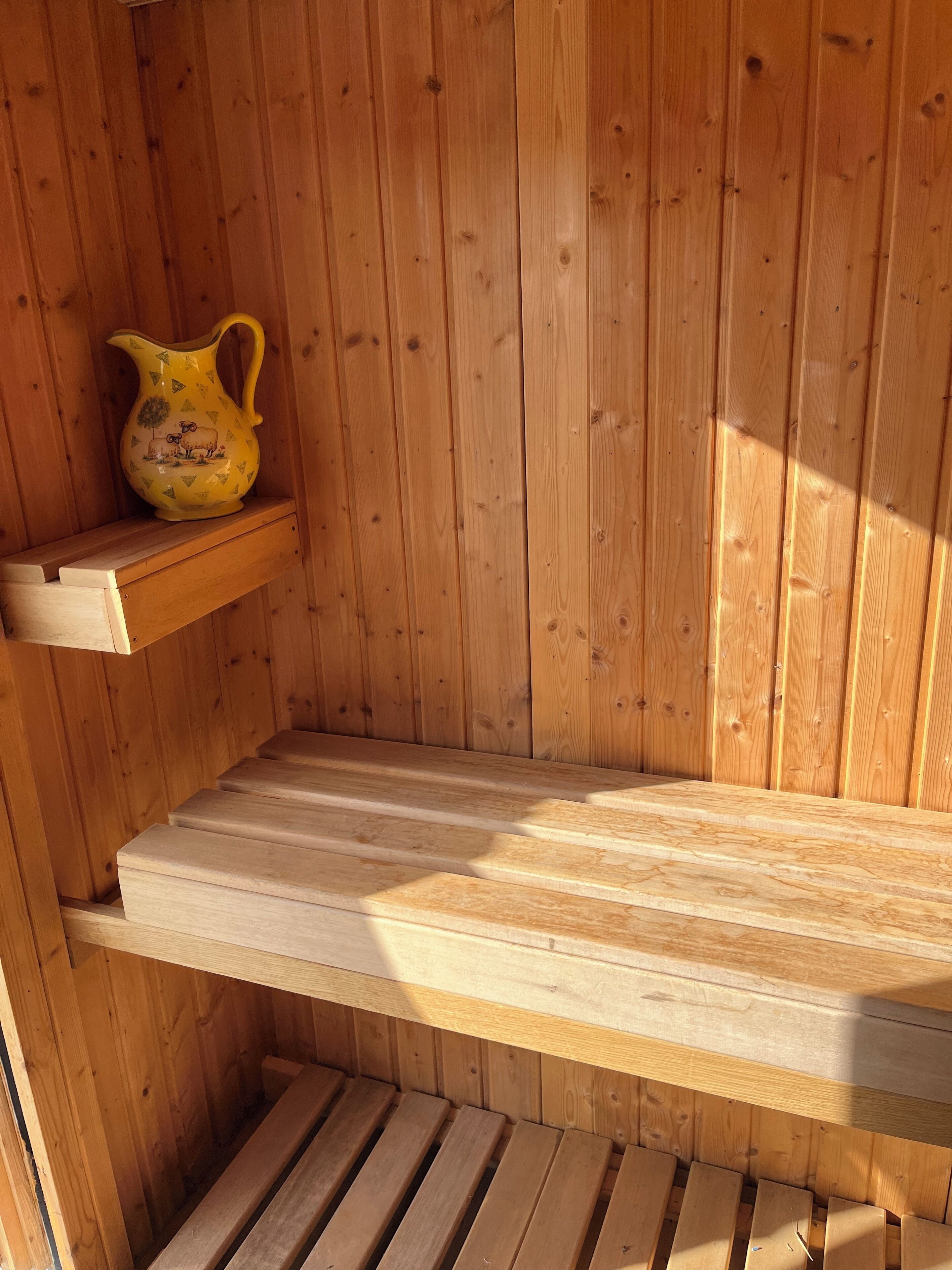 Un sauna en bois, avec un banc et une étagère sur laquelle est posé un pichet décoratif.