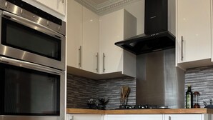 Una cocina moderna con armarios blancos, horno doble, campana extractora negra y encimera de madera.