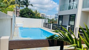 A modern residential building with a swimming pool, surrounded by greenery and palm trees. - RABBIT HOLIDAY - 8 mins walk to the beach (Flic en Flac)