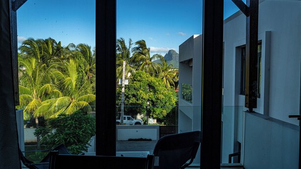 A balcony with a view of palm trees and a white building. - RABBIT HOLIDAY - 8 mins walk to the beach (Flic en Flac)