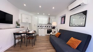Et moderne opholdsrum med spiseområde, køkken og en grå sofa med orange puder.