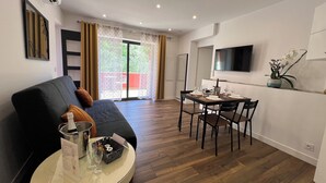 En moderne stue med sofa, spisebord dækket til to personer, tv på væggen og en skydedør til et udendørs område.