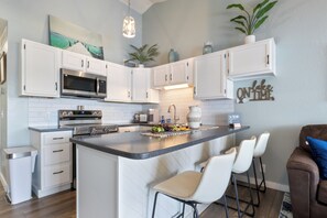 Une cuisine moderne avec des meubles blancs, un îlot central doté de tabourets, des appareils en acier inoxydable et des plantes décoratives.