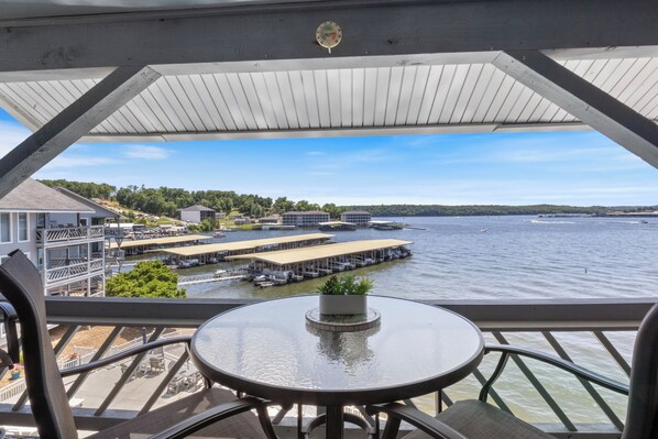 Un balcon avec une table et des chaises donnant sur une marina, où l’on peut admirer des bateaux et des quais.