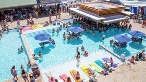 Un vaste espace extérieur avec une grande piscine et plusieurs bassins, des chaises longues et des parasols.