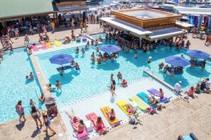 Un vaste espace extérieur avec une grande piscine et plusieurs bassins, des chaises longues et des parasols.