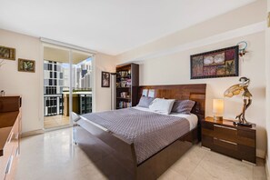 A bedroom with a large bed, a nightstand, a bookshelf, and a view of the city through a sliding door. - *LUXURY KINGDAVID*3/2C*KINGBEDROOM*BEST LOCATION* (Sunny Isles Beach)