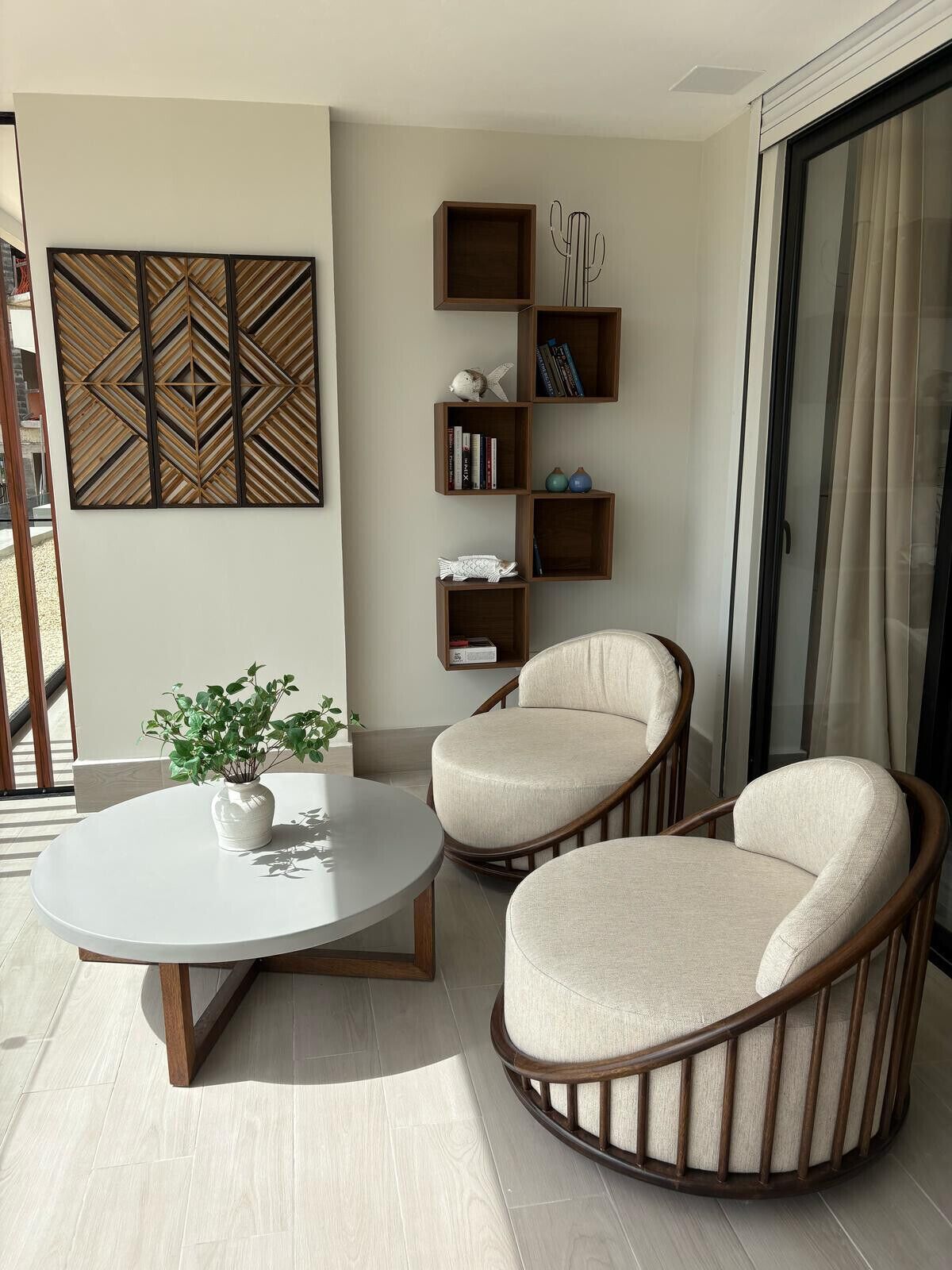 A modern living room with two beige armchairs, a round coffee table, and a decorative wall panel.