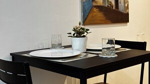 Een eettafel gedekt met borden, bestek en glazen, met een bloempot en een schilderij aan de muur.