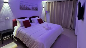 Een moderne slaapkamer met een groot bed, een nachtkastje, een televisie aan de muur en een schilderij.
