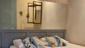 A neatly made bed with a grey blanket and pillows, a bedside table with a lamp, and a wall-mounted mirror. - Pousada & Restaurante Praeros LTDA (Rifaina)